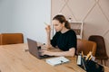 Businesswoman in headphones sits at desk, looks at laptop screen, making notes, participating in self-improvement webinar, having Royalty Free Stock Photo