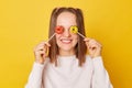 Smiling happy cheerful funky teenage girl with ponytails in jumper posing isolated over yellow background covering eyes with Royalty Free Stock Photo