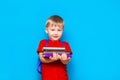 Smiling happy cute clever boy with backpack. Child with a pile of books in his hands. blue background. Ready for school. Back to