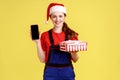 Smiling happy delivery woman holding wrapped present box and smart phone with blank screen. Royalty Free Stock Photo
