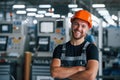 Smiling and happy employee. Portrait of industrial worker indoors in factory. Young technician with orange hard hat