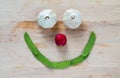 Smiling face made with garlic, radish and snow peas on a wood background