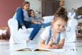 Smiling happy family sit relax on couch in living room watch little daughter drawing in album with colorful pencils