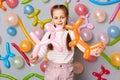 Smiling happy female kid playing at birthday party, cute little girl with braids standing against gray wall decorated with Royalty Free Stock Photo