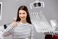 Smiling happy girl showing thumb up gesture sit at dental office chair indoor cabinet waiting stomatologist for oral procedure