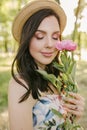 Smiling brunnete happy girl in a white-flowers dress and hat with pink peones. Sun is on the background