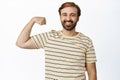 Smiling happy and healthy man showing his muscles, flexing biceps on arm, feeling strong, standing over white background