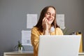 Smiling happy hipster woman working on laptop at office while talking on phone, having break, talking with friend, laughing, Royalty Free Stock Photo
