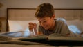 Smiling happy little cute caucasian child kid boy schoolboy reading interesting book evening in bedroom holding Royalty Free Stock Photo