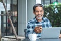 Smiling happy mature asian man with white stylish short beard using smartphone gadget serving internet at coffee shop cafe outdoor Royalty Free Stock Photo