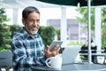 Smiling happy mature asian man with white stylish short beard using smartphone tablet serving internet at coffee shop cafe outdoor