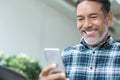 Smiling happy mature man with white stylish short beard using smartphone gadget serving internet Royalty Free Stock Photo
