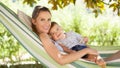 Smiling and happy mother hugs her little baby son, lying down relaxing in the hammock, in the home garden on a beautiful and sunny Royalty Free Stock Photo