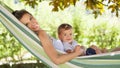 Smiling and happy mother hugs her little baby son, lying down relaxing in the hammock, in the home garden on a beautiful and sunny Royalty Free Stock Photo