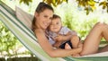 Smiling and happy mother hugs her little baby son, lying down relaxing in the hammock, in the home garden on a beautiful and sunny Royalty Free Stock Photo