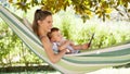 Smiling and happy mother hugs her little baby son, using smartphone, lying down relaxing in the hammock, in the home garden on a Royalty Free Stock Photo