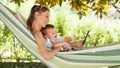 Smiling and happy mother hugs her little baby son, using smartphone, lying down relaxing in the hammock, in the home garden on a Royalty Free Stock Photo