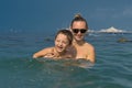 Smiling happy mother and son playing on the wave in the sea in t