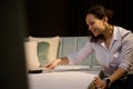 Smiling happy multiethnic saleswoman in furniture store using brush to clean dust from orthopedic mattress on soft sofa bed