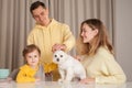 Smiling happy parents with child son and white dog, three abstract plastic bottles on the table