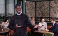 Smiling politely African American chef inviting to visit cozy restaurant