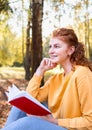 Smiling happy red hair student girl reading a book outside in autumn park Royalty Free Stock Photo