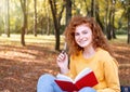 Smiling happy red hair student girl taking a note outside in autumn park