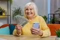 Smiling happy senior grandmother woman counting money cash use smartphone, income saves, lottery win Royalty Free Stock Photo