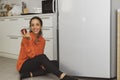 Smiling happy Spanish woman holding apples sitting in front of kitchen refrigerator. Royalty Free Stock Photo