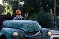 Smiling, happy, welcoming, fun friendly pumpkin head scarecrow driving an old truck to a halloween harvest party