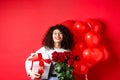 Smiling happy woman holding box with gift and red roses from boyfriend, celebrating Valentines day, standing near Royalty Free Stock Photo
