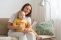 Smiling and happy woman sitting on sofa with adorable baby in light living room Royalty Free Stock Photo