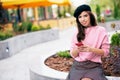 Smiling happy woman standing outdoors texting on mobile phone. Young brunette female wears pink sweater and black beret resting Royalty Free Stock Photo