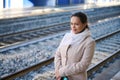 Smiling happy woman in warm beige coat standing outdoor on the platform of a railway station, waiting to board the train Royalty Free Stock Photo
