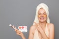 Smiling happy woman wrapped in towel standing cosmetics brushes and palette of eye shadows in hands, pointing away at