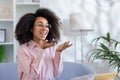 A smiling and happy young African American woman is sitting on the couch at home in a pink shirt, holding a phone in her Royalty Free Stock Photo