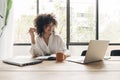 Smiling, happy, young african american woman studying at home with laptop. Taking notes in notebook. Bright living room. Royalty Free Stock Photo