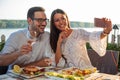 Smiling happy young couple posing for a selfie, eating dinner in a riverside restaurant Royalty Free Stock Photo