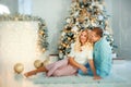 Smiling happy young married couple wife and husband sitting near christmas tree with christmas lights around. Boyfriend and Royalty Free Stock Photo
