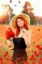 Smiling and happy young red-haired  woman in a black dress and a hat holding red poppies near the face. Beautiful poppy field at Royalty Free Stock Photo