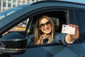 smiling young woman showing her new driver license out of car window after successful test at driving school Royalty Free Stock Photo