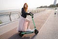 Smiling happy young woman using electric scooter in big city bridge.