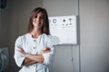 Smiling and having good mood. Beautiful female doctor standing in the office with hands crossed and pictures at Royalty Free Stock Photo