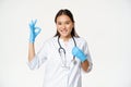 Smiling healthcare worker, asian woman doctor in rubber gloves and medical uniform, shows approval, okay sign, white Royalty Free Stock Photo