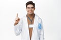 Smiling healthcare worker in robe, pointing finger up, showing advertisement, clinic promo, standing over white Royalty Free Stock Photo