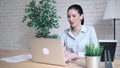 Smiling hipster girl talking and waving and Hello during a video call with a laptop sitting at the table at work