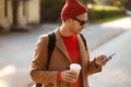 Smiling hipster man wear sunglasses using cellphone standing at the street drinking takeaway coffee Royalty Free Stock Photo