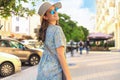 Smiling hipster trendy girl posing at the city summer street,holding hat. Royalty Free Stock Photo