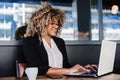 Smiling hispanic afro business woman wearing eye glasses in cafe using laptop and mobile phone Royalty Free Stock Photo