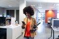 Smiling hispanic businesswoman walking while using smartphone at modern workplace Royalty Free Stock Photo